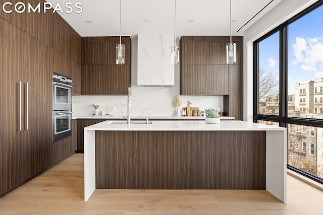 kitchen featuring light hardwood / wood-style flooring, decorative light fixtures, sink, a center island with sink, and stainless steel double oven