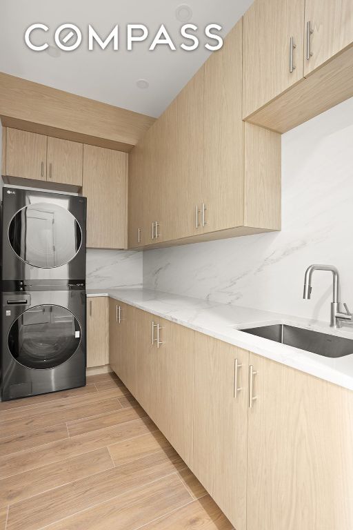 kitchen featuring light wood finished floors, decorative backsplash, stacked washer / dryer, light brown cabinetry, and a sink