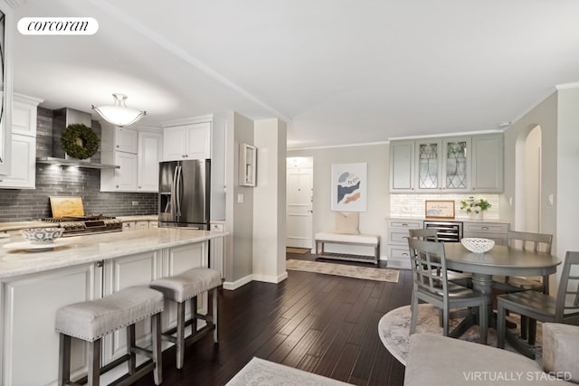 kitchen with appliances with stainless steel finishes, white cabinets, dark hardwood / wood-style flooring, light stone counters, and wall chimney exhaust hood