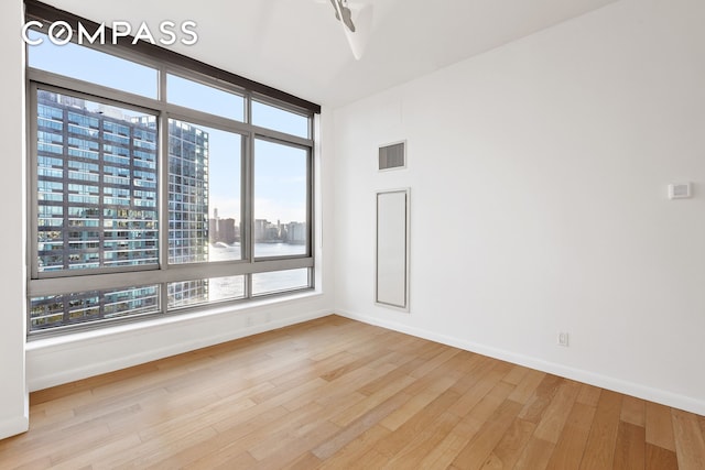 empty room with visible vents, a city view, baseboards, and wood finished floors