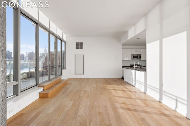 unfurnished living room featuring a water view, sink, and light hardwood / wood-style floors