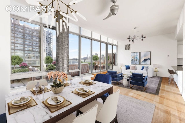 dining area with light wood-type flooring, a view of city, a chandelier, and a wall of windows