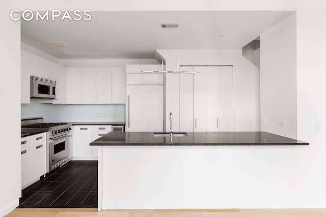 kitchen with dark countertops, visible vents, white cabinetry, a sink, and high quality appliances