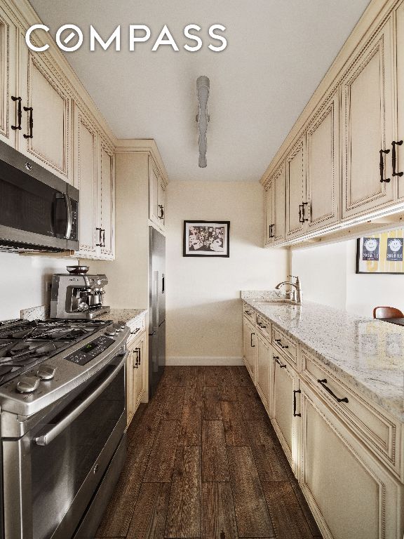 kitchen featuring light stone countertops, dark wood-type flooring, stainless steel appliances, and cream cabinetry