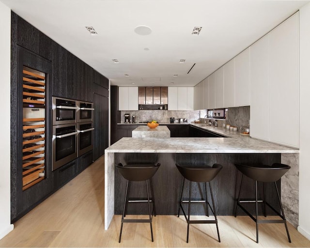 kitchen with light hardwood / wood-style flooring, white cabinets, a kitchen bar, decorative backsplash, and kitchen peninsula