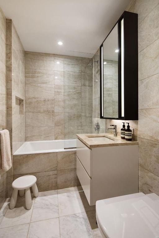 bathroom featuring tile walls, vanity, tiled bath, and toilet