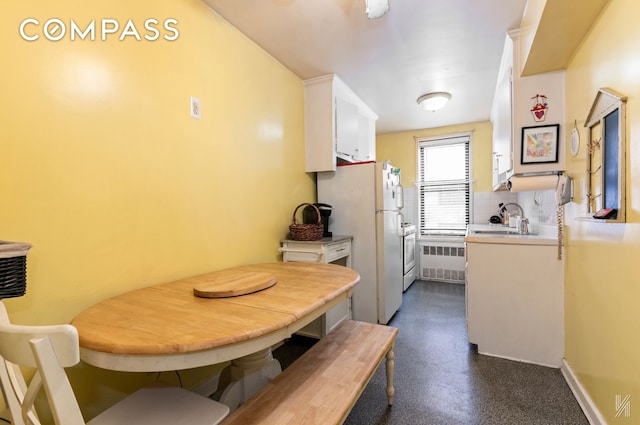 kitchen with light countertops, radiator heating unit, freestanding refrigerator, white cabinetry, and a sink