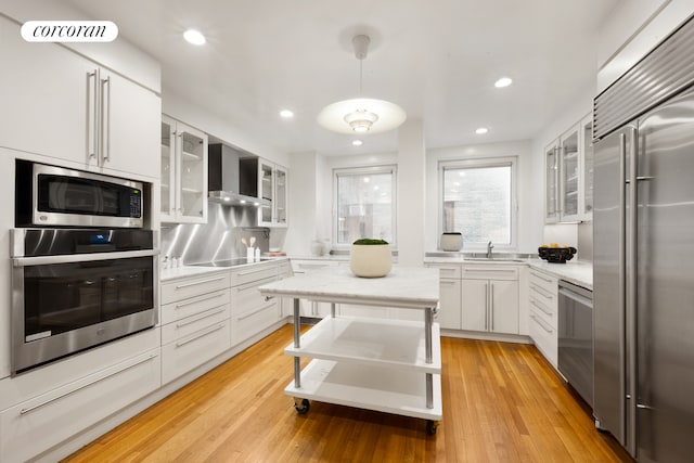 1158 5th Ave Unit 9/10A, New York City, NY 10029 - kitchen featuring stainless steel appliances, wall chimney exhaust hood, a sink, white cabinetry, and recessed lighting