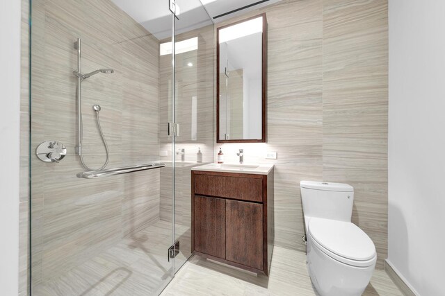 bathroom with toilet, a shower stall, tile walls, and vanity