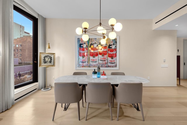 dining space with an inviting chandelier, baseboard heating, and light wood finished floors