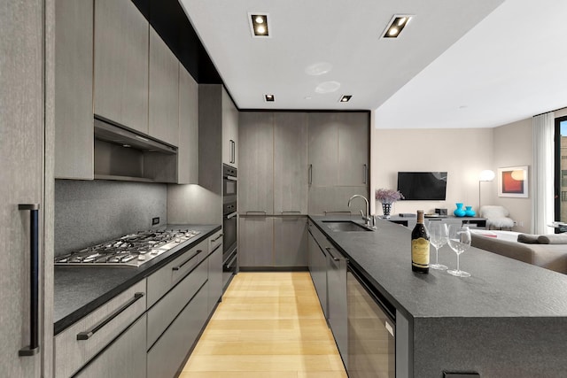 kitchen featuring dark countertops, stainless steel gas cooktop, a sink, a peninsula, and open floor plan