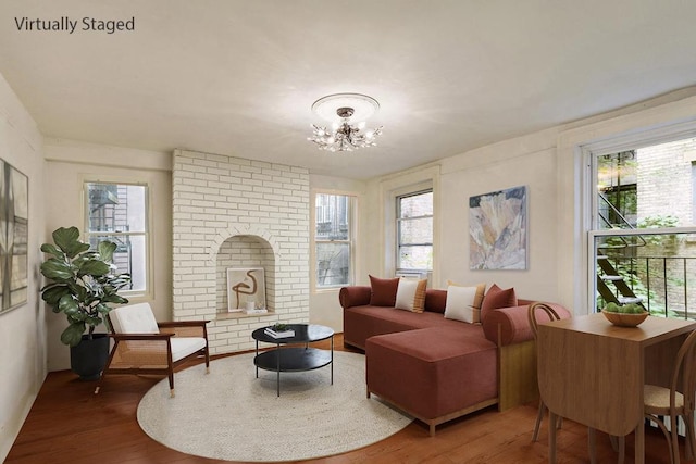 living area with hardwood / wood-style flooring, a brick fireplace, and a notable chandelier