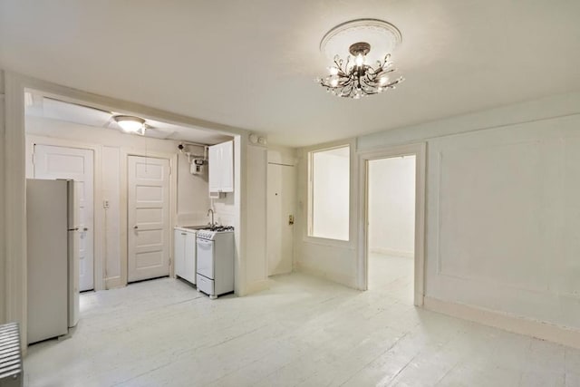 kitchen with sink, a chandelier, fridge, white gas range, and white cabinets