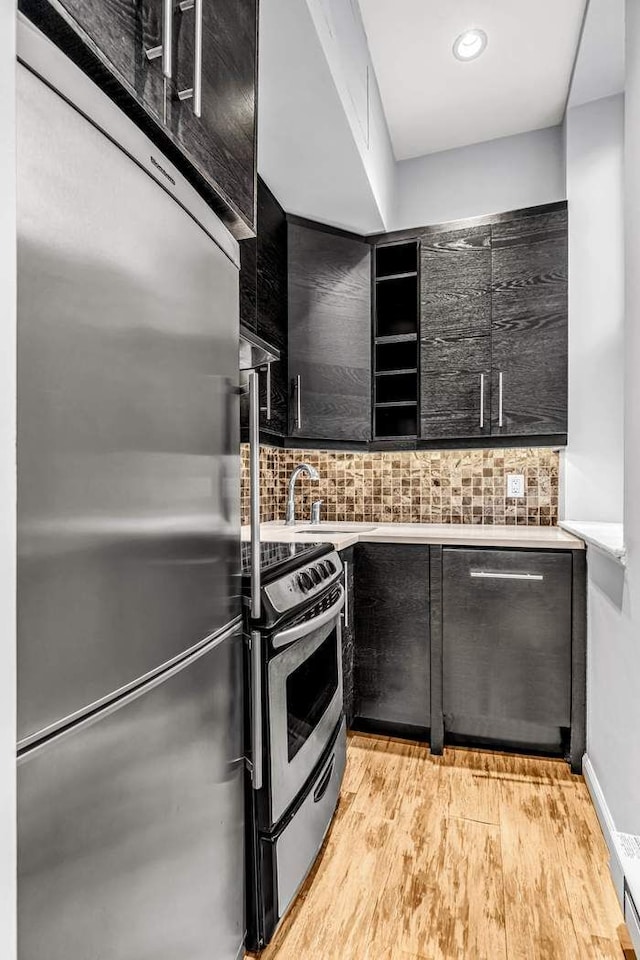 23 Waverly Pl Unit 3B, New York City, NY 10003 - kitchen featuring stainless steel appliances, dark cabinetry, tasteful backsplash, open shelves, and light wood-type flooring