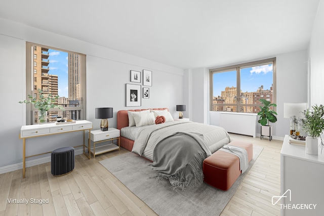 bedroom with a view of city, light wood finished floors, and baseboards