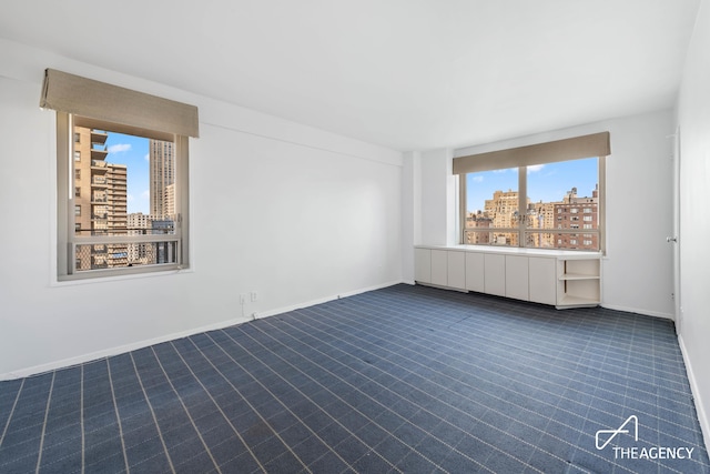 spare room with dark colored carpet, a city view, and baseboards