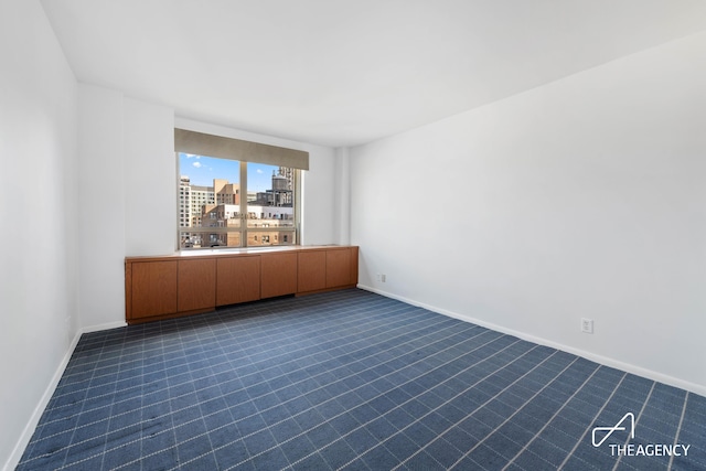 unfurnished room featuring baseboards, a view of city, and dark carpet