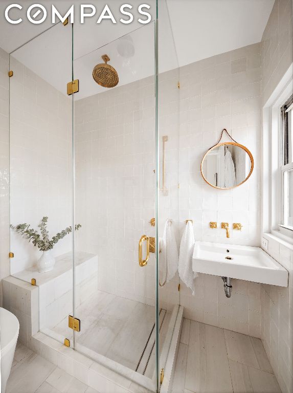 bathroom with walk in shower, sink, and tile walls