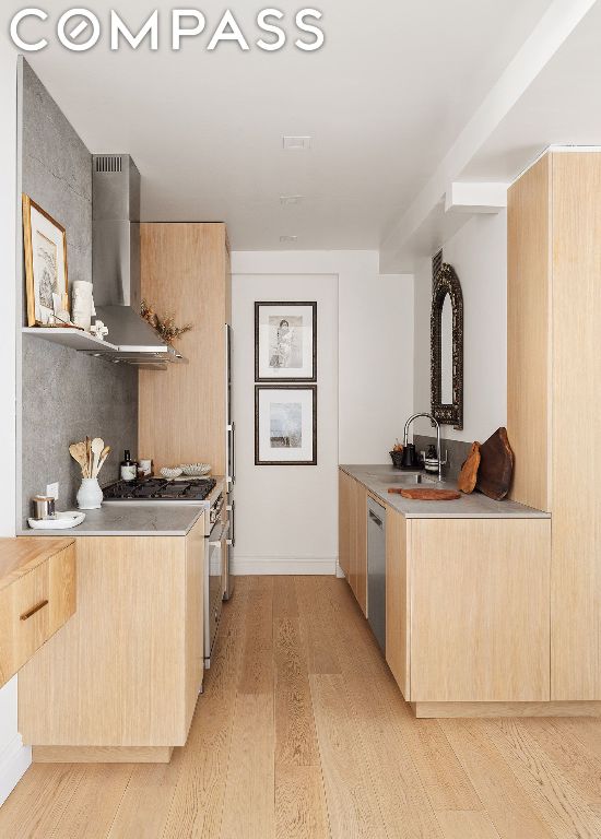 kitchen featuring wall chimney exhaust hood, sink, light hardwood / wood-style flooring, light brown cabinets, and dishwasher