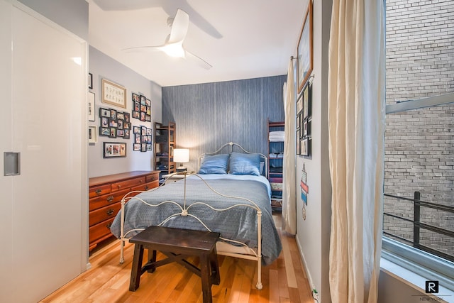 bedroom with ceiling fan, an accent wall, and light wood-style flooring