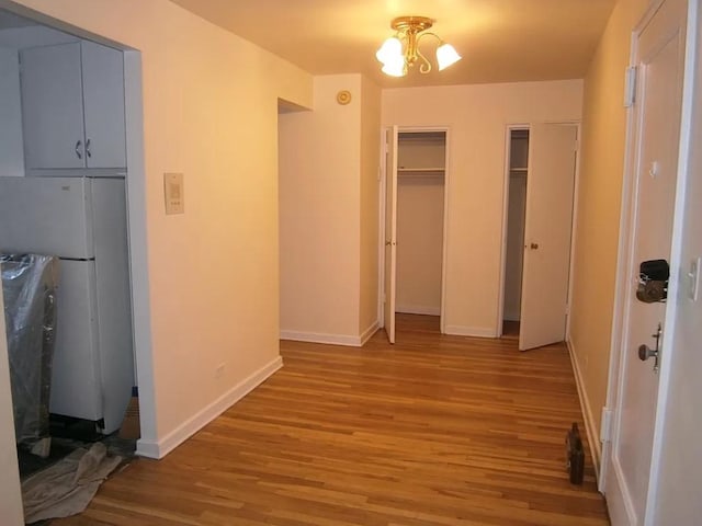 unfurnished bedroom with an inviting chandelier, white refrigerator, and light wood-type flooring