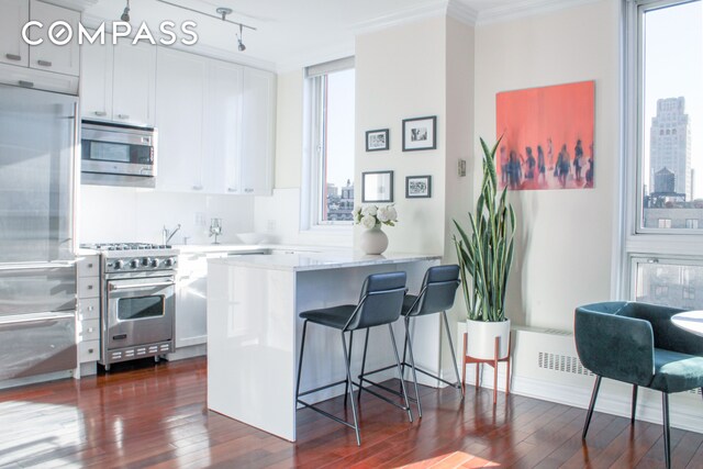 kitchen featuring a breakfast bar area, white cabinets, kitchen peninsula, stainless steel appliances, and a healthy amount of sunlight