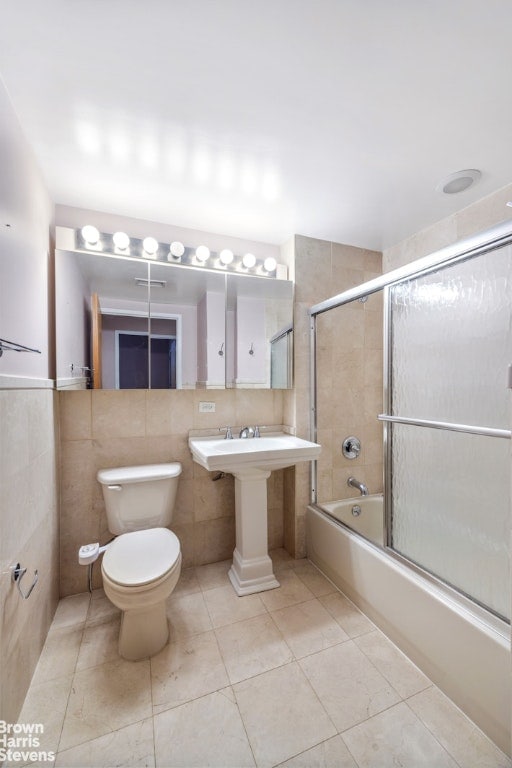 bathroom with shower / bath combination with glass door, toilet, and tile walls