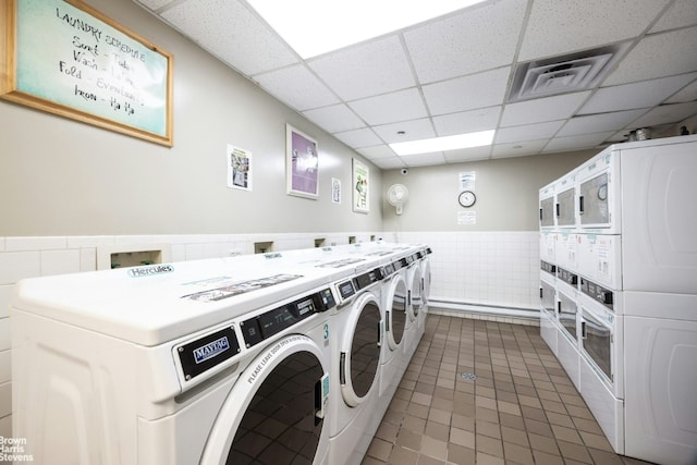 laundry area with stacked washer / drying machine, dark tile patterned flooring, washing machine and dryer, and tile walls