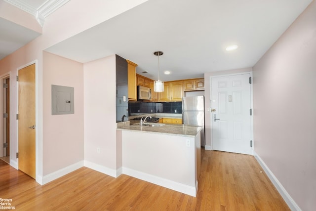 kitchen with appliances with stainless steel finishes, decorative light fixtures, tasteful backsplash, kitchen peninsula, and light wood-type flooring