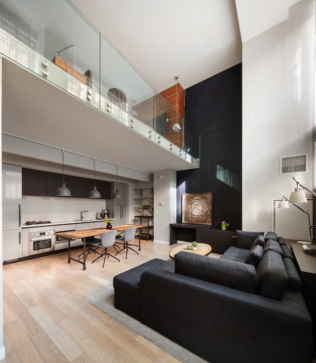 living area featuring visible vents, light wood-style floors, and a towering ceiling