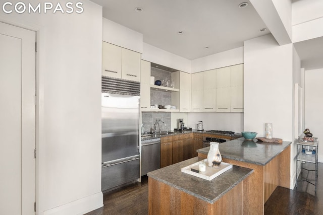 kitchen featuring sink, dark wood-type flooring, stainless steel appliances, decorative backsplash, and kitchen peninsula