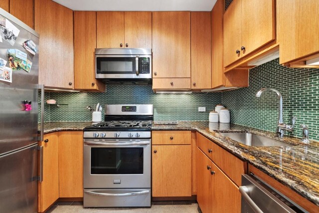 kitchen with dark stone countertops, sink, decorative backsplash, and appliances with stainless steel finishes