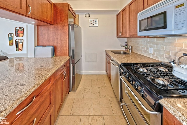 kitchen with tasteful backsplash, appliances with stainless steel finishes, sink, and light stone counters