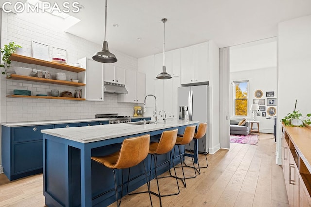 kitchen featuring stainless steel refrigerator with ice dispenser, blue cabinets, an island with sink, and white cabinets