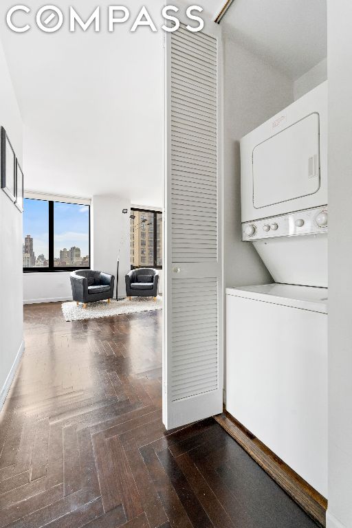 clothes washing area with stacked washer / dryer and dark parquet floors