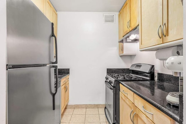 kitchen featuring light tile patterned flooring, dark stone countertops, appliances with stainless steel finishes, and light brown cabinetry