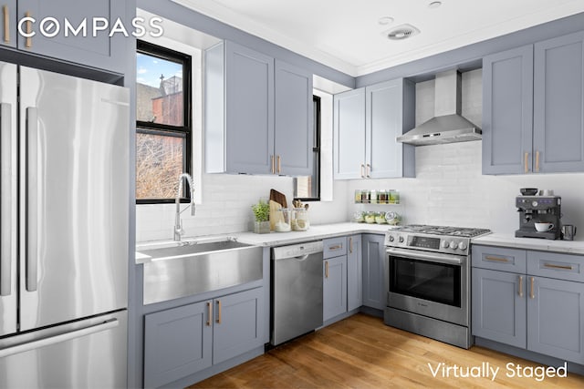 kitchen with tasteful backsplash, wall chimney exhaust hood, appliances with stainless steel finishes, light wood-style floors, and a sink