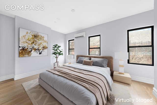 bedroom with baseboards, light wood finished floors, and a wall mounted AC