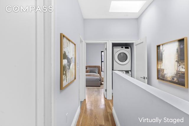 hallway with light wood-style floors, stacked washer / drying machine, baseboards, and a skylight