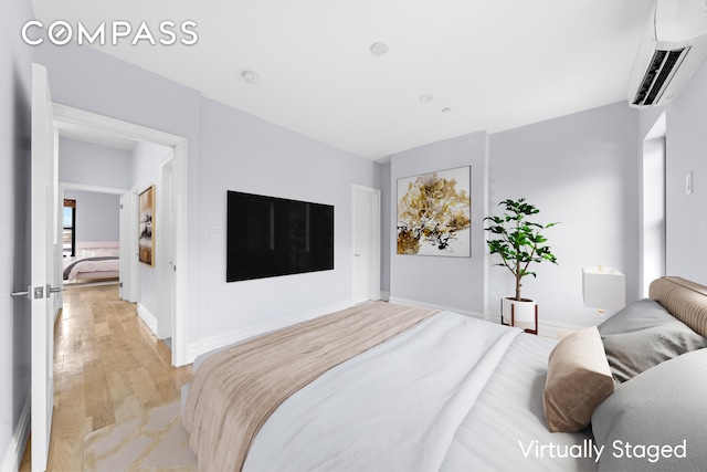 bedroom with baseboards, a wall unit AC, and light wood finished floors