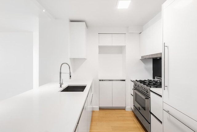 kitchen with sink, built in refrigerator, light hardwood / wood-style flooring, stainless steel range with gas cooktop, and white cabinets