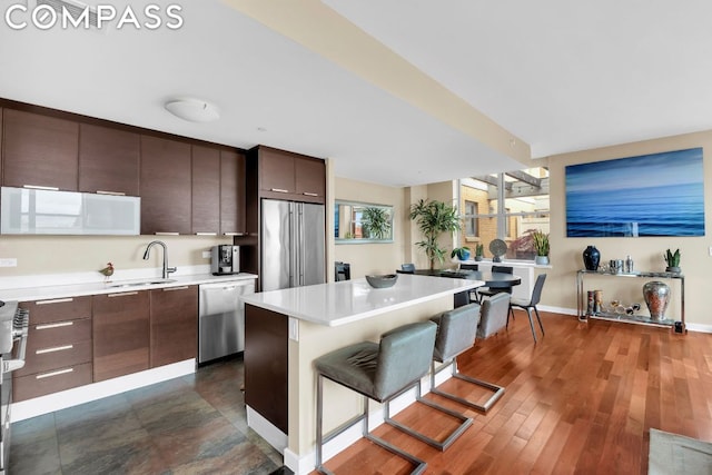 kitchen with sink, a kitchen breakfast bar, stainless steel appliances, a center island, and dark brown cabinetry