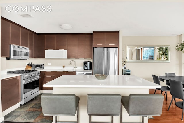 kitchen with light countertops, a breakfast bar area, dark brown cabinetry, and stainless steel appliances