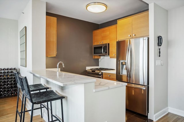 kitchen featuring appliances with stainless steel finishes, a breakfast bar, dark hardwood / wood-style flooring, kitchen peninsula, and light stone countertops