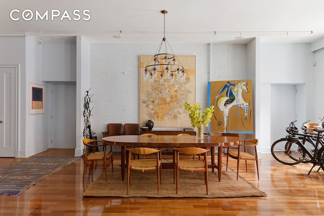 dining space with brick wall, track lighting, and wood finished floors