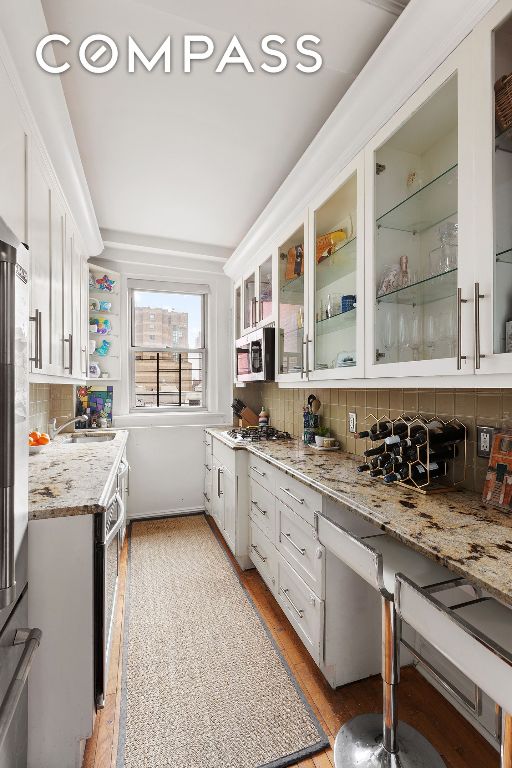 kitchen featuring decorative backsplash, glass insert cabinets, appliances with stainless steel finishes, white cabinets, and light stone countertops