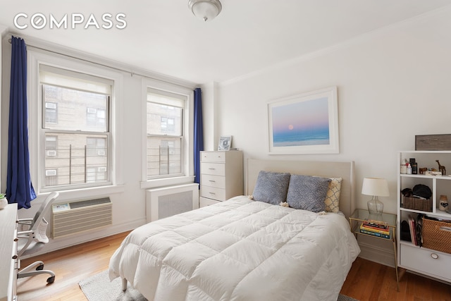 bedroom featuring crown molding, a wall mounted AC, and wood finished floors