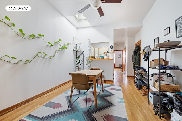 office space featuring a skylight, baseboards, ceiling fan, and light wood finished floors