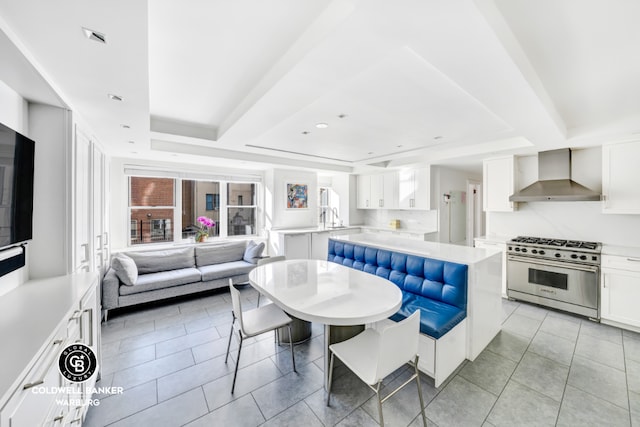 kitchen featuring light tile patterned floors, a tray ceiling, high end stainless steel range oven, wall chimney range hood, and white cabinets