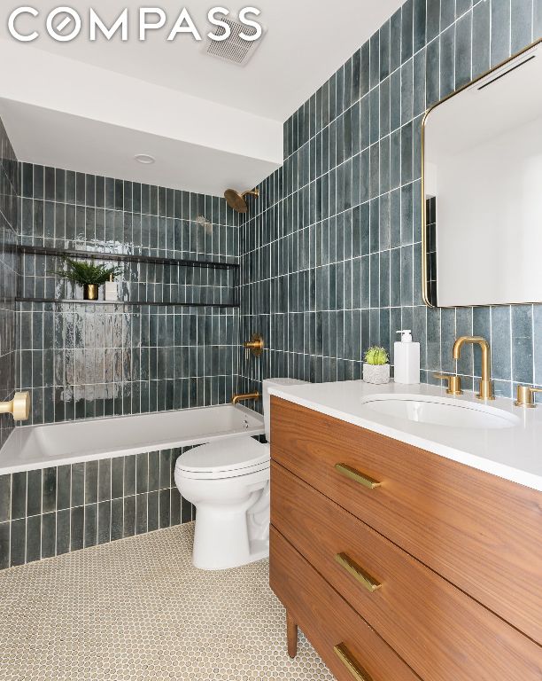 full bathroom featuring tile walls, vanity, tiled shower / bath, tile patterned floors, and toilet